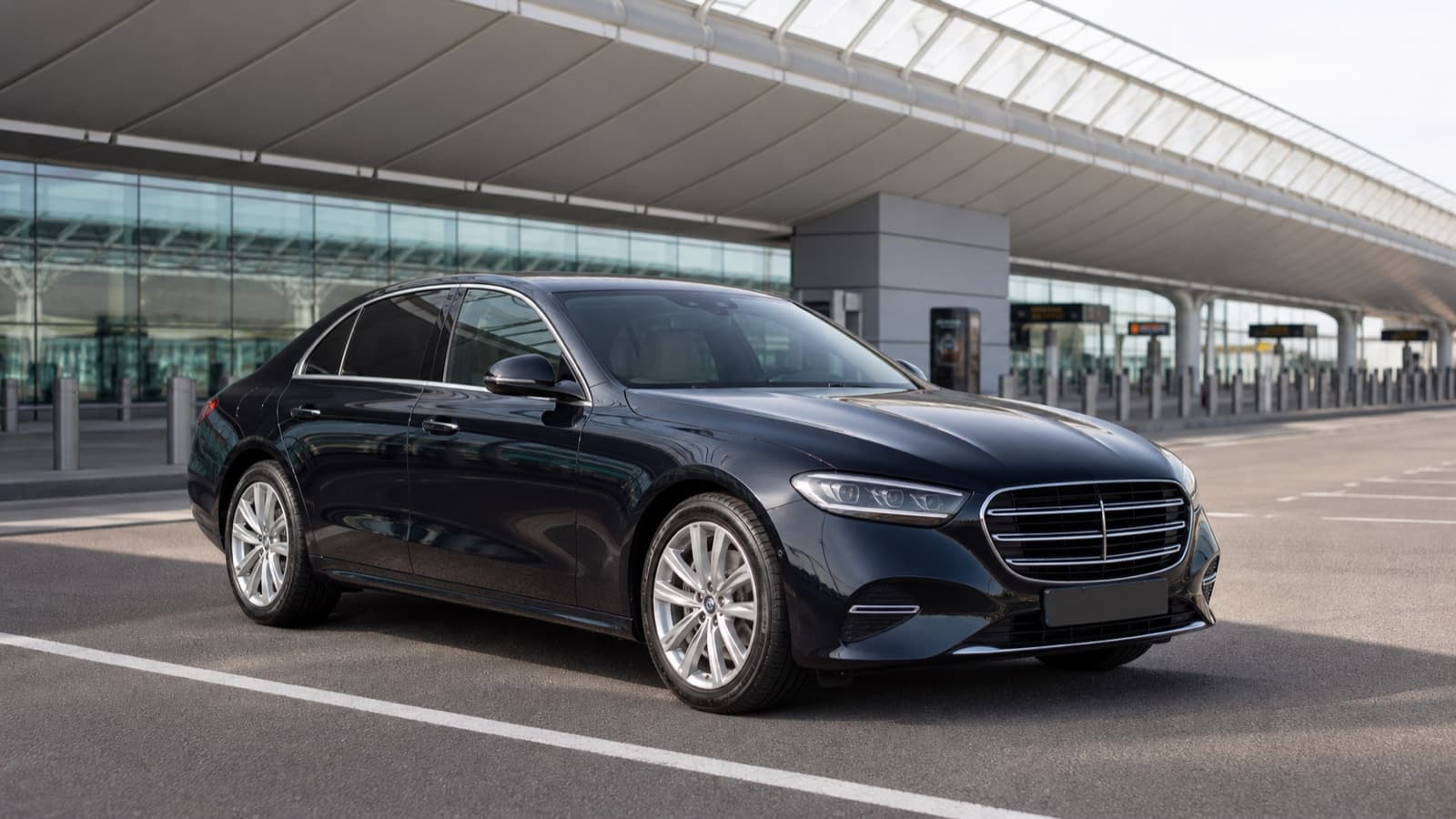 Black executive airport transfer sedan at a terminal pickup lane