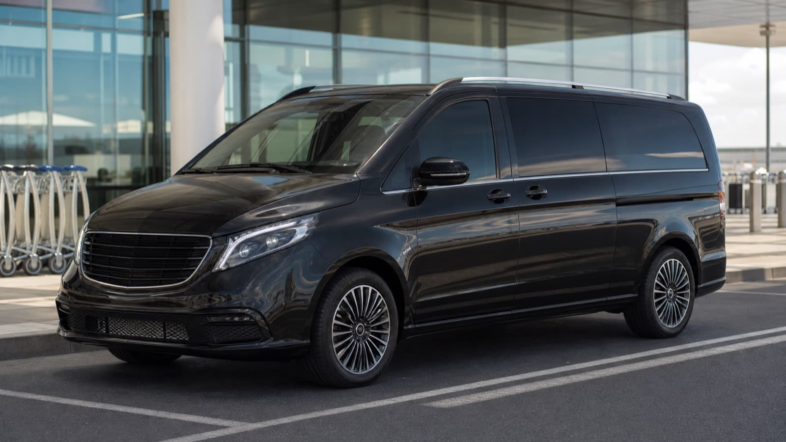 Black passenger transfer van at an airport pickup lane